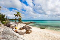 Uno scorcio panoramico sulla spiaggia tropicale dell'isola di Eleuthera, Bahamas, con ombrelloni in paglia, panche e sedie in legno.

