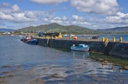 Il vecchio muro del porto a Knightstown, Valentia Island, Irlanda. Imbarcazioni da diporto e barche da pesca ormeggiate nel porto sono incorniciate da un cielo blu con soffici nuvole che si ...
