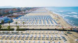 Veduta aerea del litorale di Lido di Camaiore con ombrelloni e sdraio di vari colori per indicare i differenti bagni, Lucca, Toscana.



