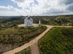 Veduta aerea di un vecchio mulino a vento in disuso con la città di Silves sullo sfondo, Portogallo.

