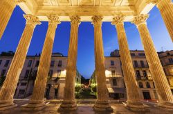 Veduta by night del centro di Nimes attarverso le colonne della Maison Carrée di Nimes, Francia.
