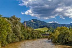 Veduta del fiume Mura e di una chiesa a Leoben, Austria. A fare da cornice è una natura verde e rigogliosa.



