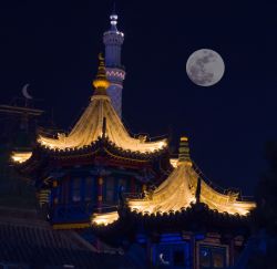 Veduta notturna di tetti in una strada islamica di Hohhot, capitale della Mongolia Interna, Cina. Sullo sfondo, una suggestiva luna piena.

