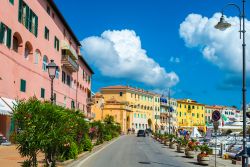 Veduta panoramica di una strada di Portoferraio, isola d'Elba, con edifici e il porto.

