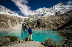 Un viaggiatore avventuroso con zaino in spalla contempla la laguna dai 69 colori allo Huascaran National Park, Huaraz, Perù. Sullo sfondo, la grande montagna Chacraraju innevata. Il parco ...