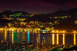 Vista serale di Lerici (La Spezia), con il porto in primo piano e la cittadina illuminata che si riflette sull'acqua.
