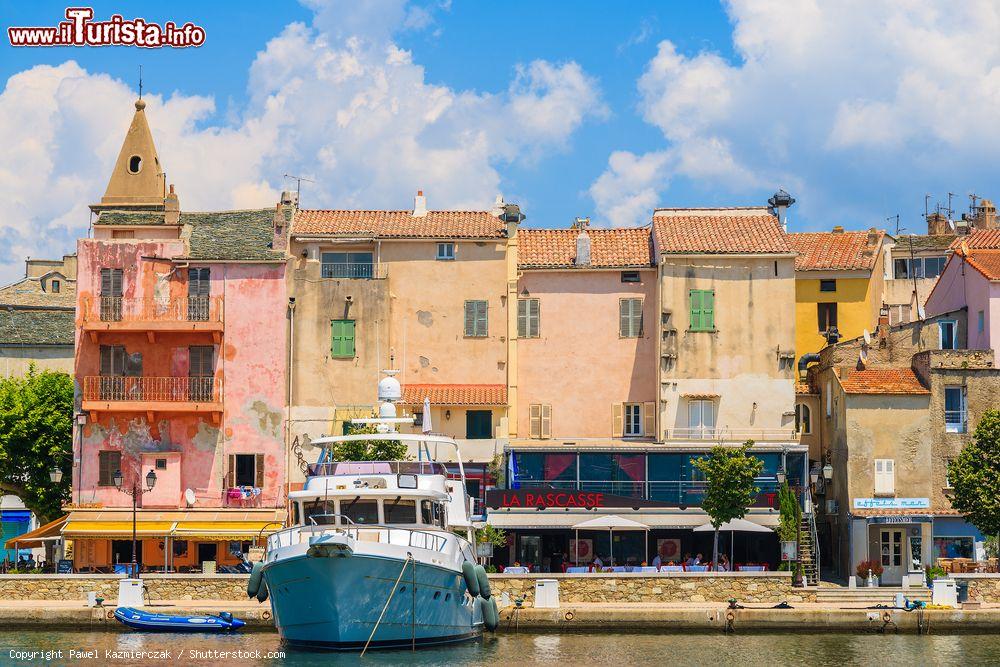 Immagine Piccolo porto di pescatori a Saint Florent, Corsica, Francia. Le abitazioni dalle facciate color pastello si rispecchiano sulle acque del porto dove sono ormeggiate le imbarcazioni su cui viaggiano i turisti. - © Pawel Kazmierczak / Shutterstock.com
