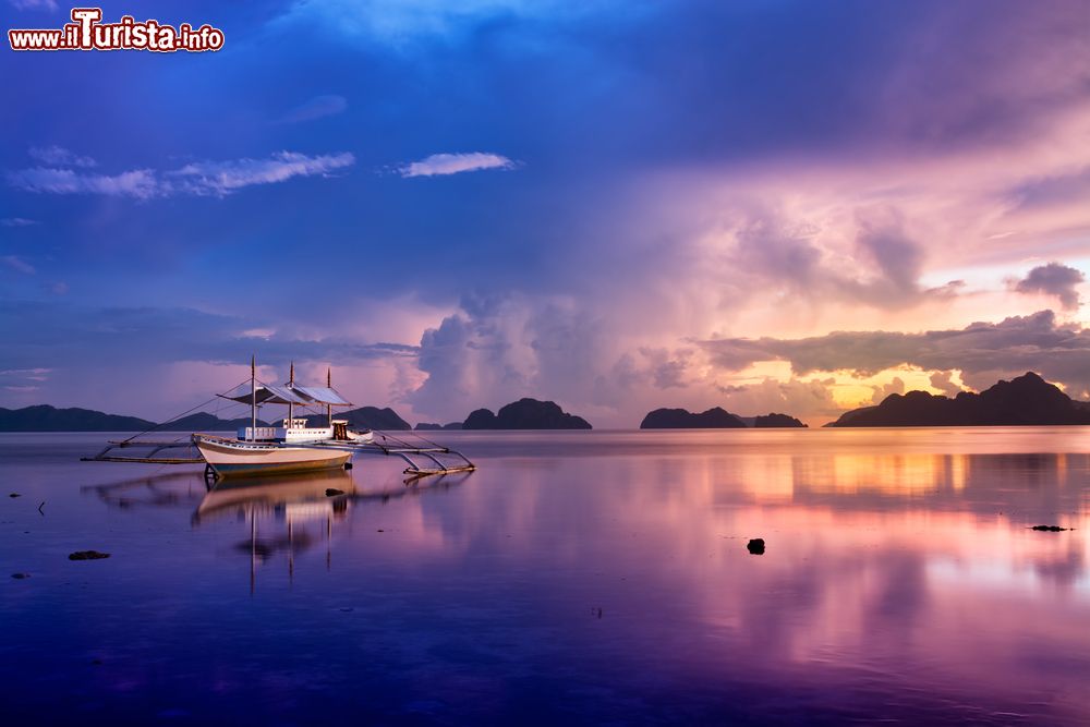 Immagine Un pittoresco tramonto sulla baia di El Nido, isola di Palawan, Filippine. In primo piano, una tradizionale barca in legno.