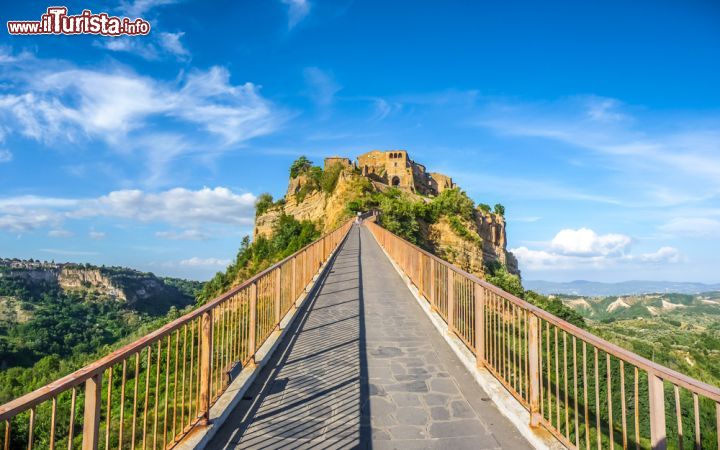 Immagine Il ponte di Civita di Bagnoregio, Lazio, collega il borgo a Bagnoregio e al resto del mondo. Ricostruito due volte dopo l'abbattimento della vecchia struttura in muratura fatta saltare dai tedeschi durante la Seconda Guerra Mondiale, il viadotto è un sottilissimo e lungo camminamento in cemento che permette di raggiungere quella che da decenni viene definita e pubblicizzata come la "città che muore". Nel 1964, quando alcuni smottamenti colpirono queste colline, il ponte mal costruito crollò poco prima dell'inaugurazione ufficiale; fatto ricostruire con le adeguate norme di sicurezza, oggi il ponte è percorso dai tanti turisti che si recano in visita a questo suggestivo borgo che pian piano si sta ripopolando - © canadastock / Shutterstock.com