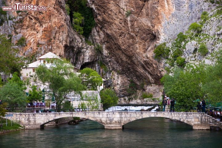 Immagine Un ponte sul fiume Buna a Blagaj: al cospetto della montagna - il fiume Buna nasce da una montagna a Blagaj e, dopo un precipizio di 200 metri, scorre lungo il territorio del cantone Erzegovina-Narenta, nell'estremo sud della Bosnia. Il passaggio del fiume in contrasto alle alti pareti rocciose, i colori naturali impressionanti creati da questa combinazione e la curiosa posizione del villaggio, rendono Blagaj uno dei posti più famosi di tutta la Bosnia-Erzegovina. - © Hieronymus / Shutterstock.com