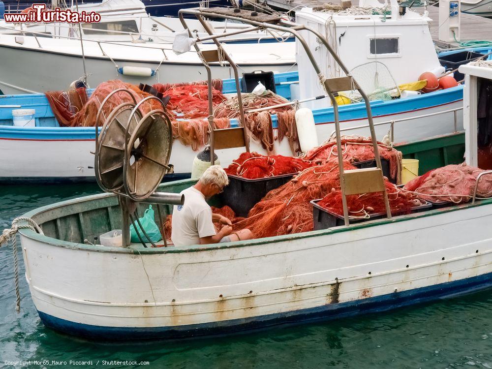 Immagine Porto di Oneglia, Imperia: un pescatore sistema le reti sulla sua barca - © Mor65_Mauro Piccardi / Shutterstock.com