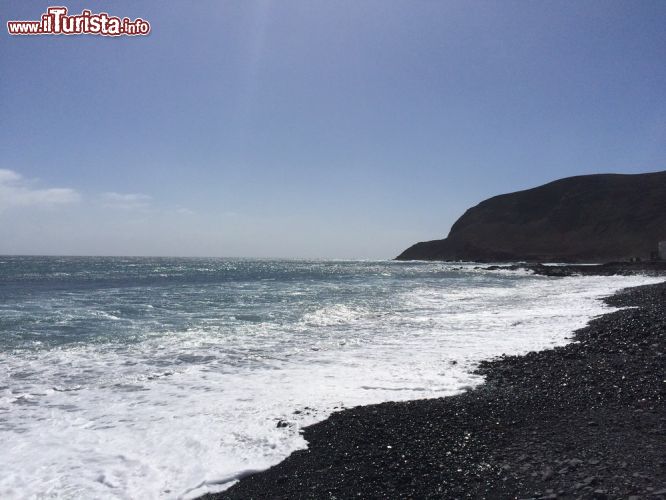 Immagine Vista panoramica di Pozo Negro e la sua spiaggia a Fuerteventura (Spagna) - Un mare tranquillo, quasi privo di vento e correnti marine o alte maree: questa è l'acqua di Pozo Negro, sita vicino a El Muellito. Come si vede nell'immagine i sassolini neri che sono presenti al posto della sabbia, qui sono una vera e propria specialità della spiaggia, come tutta la baia del resto, che si distingue con eleganza da tutte le altre coste di Fuerteventura.