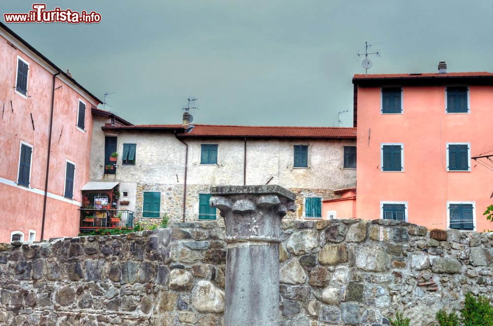 Immagine Resti di un'antica colonna nel centro di Brugnato, La Spezia, Italia. Sullo sfondo le abitazioni dalle facciate color pastello della cittadina.