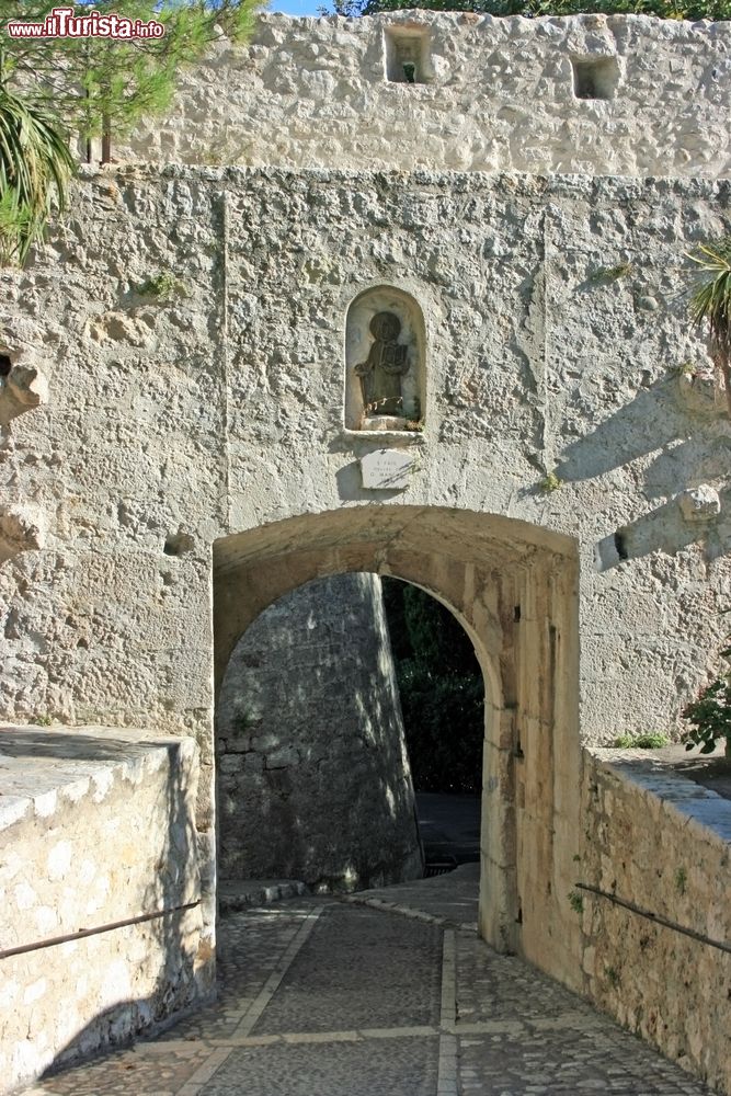 Immagine Uno scorcio della città castello di Saint-Paul-de-Vence, Francia. La strada acciottolata attraversa l'arco di uscita dalle mura in cui si trova una statua di San Paolo.