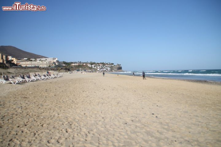 Immagine Fotografia della spiaggia di Morro Jable, Fuerteventura, Spagna - Quando la flotta peschereccia di Morro Jable partiva da qui, ancora non immaginava sarebbe diventata una delle spiagge più belle di Fuerteventura e non solo. Qui infatti sorgono moltissimi hotel che ospitano tutti i turisti che non vedono l'ora di camminare sulla sabbia bianca che si estende per ben quattro chilometri in uno spazio meravigliosamente estivo, fatto del colore turchese delle acque e del blu intenso del cielo.