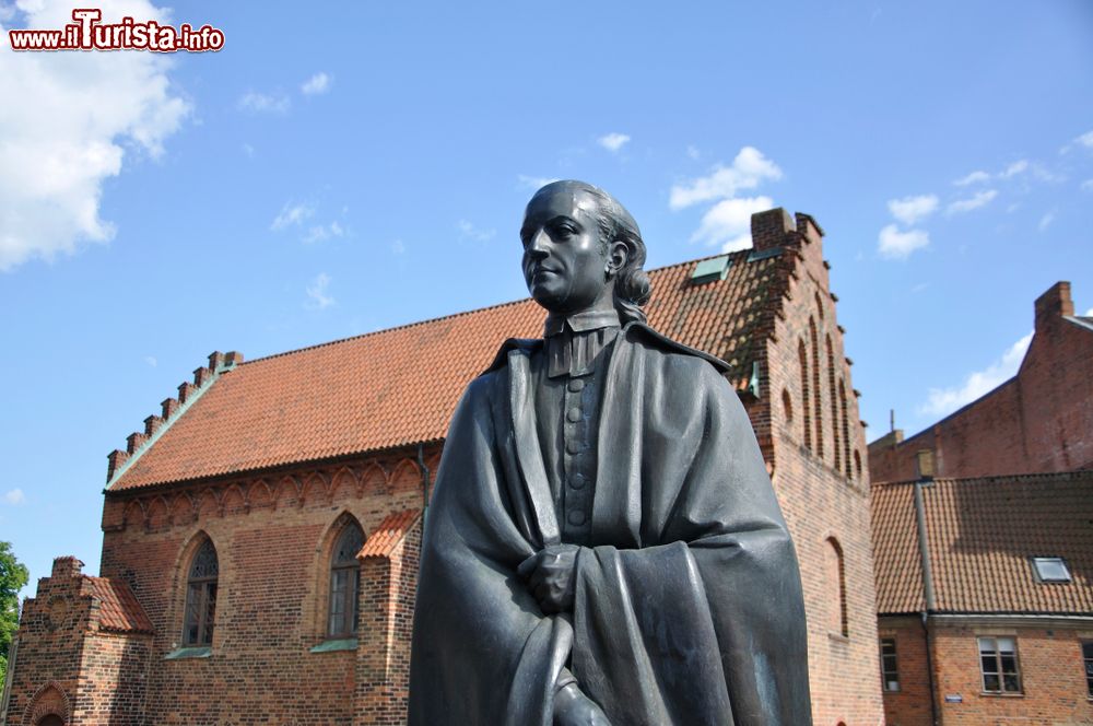 Immagine La statua di Heuric Schartou a Lund (Svezia) con l'edificio religioso del Liberiet sullo sfondo.