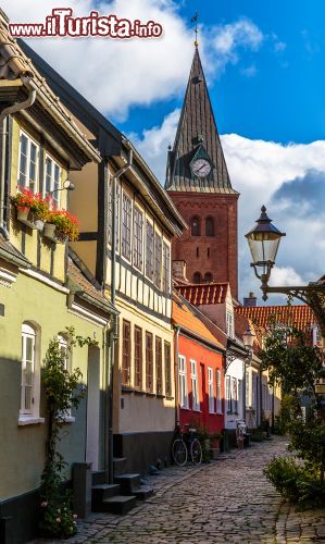 Immagine Una strada acciottolata nel centro storico di Aalborg (Danimarca) si insinua tra le case colorate e il campanile della chiesa alle loro spalle - © foto Anders Riishede / Shutterstock.com