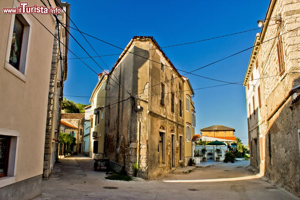 Immagine Strada del centro storico di Susak, Croazia. Sull'isola c'è un solo paese, dove vivono circa 180 abitanti. Tra i suoi eventi il Festival Musicale Internazionale, animato da diversi concerti. Il Susak Air+Art Festival differisce completamente, essendo esso dedicato ai costruttori e guidatori di aquiloni per un evento all’insegna del divertimento e della spensieratezza, organizzato a cadenza biennale. La Processione del Corpus Christi si svolge ogni 15 luglio attraverso appunto una processione che inizia e termina alla Chiesa di San Nicola.