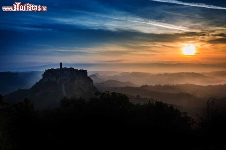 Immagine Tramonto su Civita di Bagnoregio, Viterbo. Il borgo rossiccio di Civita, su cui spicca l'esile campanile romanico della chiesa, si erge come un'isola nel mare di calanchi, creste d'argilla dalle forme ondulate, modellati dall'acqua e dal vento. Situata al confine con l'Umbria, questa località della provincia viterbese si adagia su un colle di tufo cuneiforme a 443 metri sul livello del mare, stretto fra due profondi burroni, quello del Rio Torbido e quello del Rio Chiaro - © 234355087 / Shutterstock.com