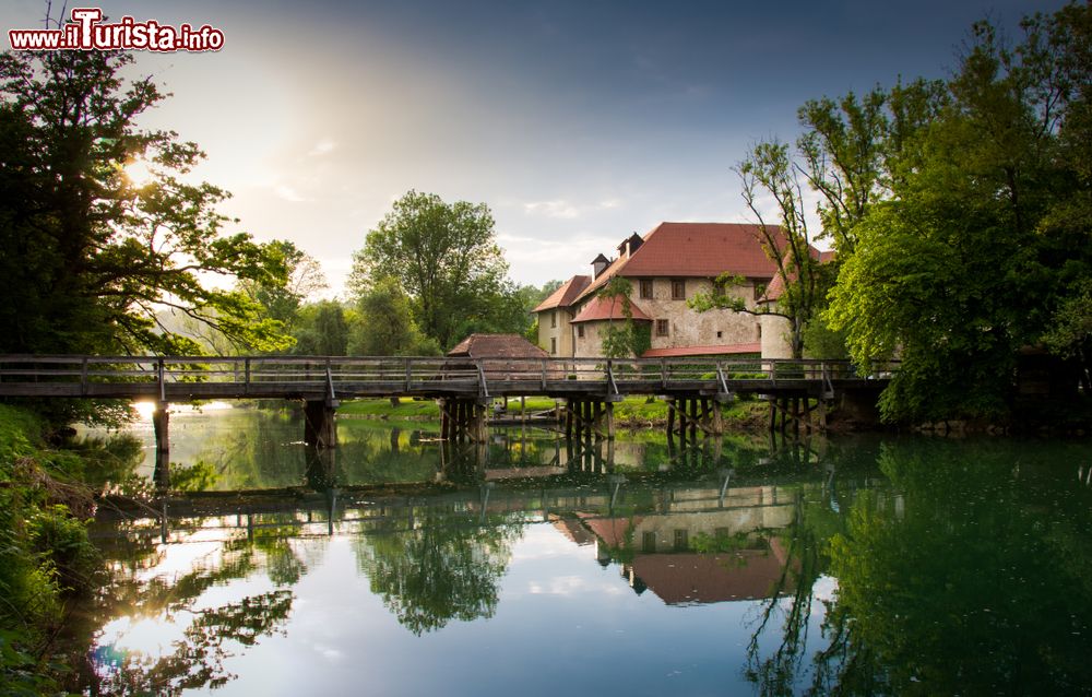 Immagine Tramonto sul castello di Otocec, Slovenia, con un ponte in legno sul fiume Krka. Siamo in uno dei luoghi più suggestivi e ricchi di fascino della Slovenia.