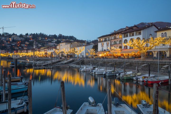 Immagine Tramonto sul lago durante il periodo natalizio a Ascona, Svizzera. Una bella immagine del lungolago di Ascona con le decorazioni e le luminarie che addobbano strade e locali durante il Natale - © RnDmS / Shutterstock.com