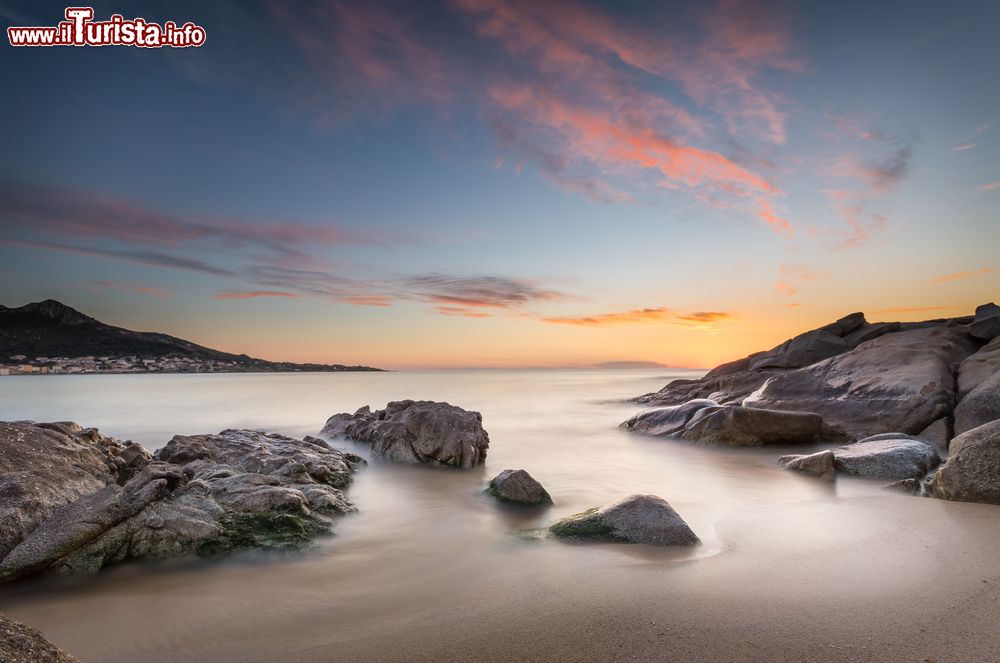 Immagine Tramonto sulle rocce nella spiaggia di Algajola, Corsica. Questo piccolo villaggio fortificato è una meta vacanziera scelta da francesi e anche da italiani che vedono in Algajola una sorta di gemella di destinazioni della Sardegna.