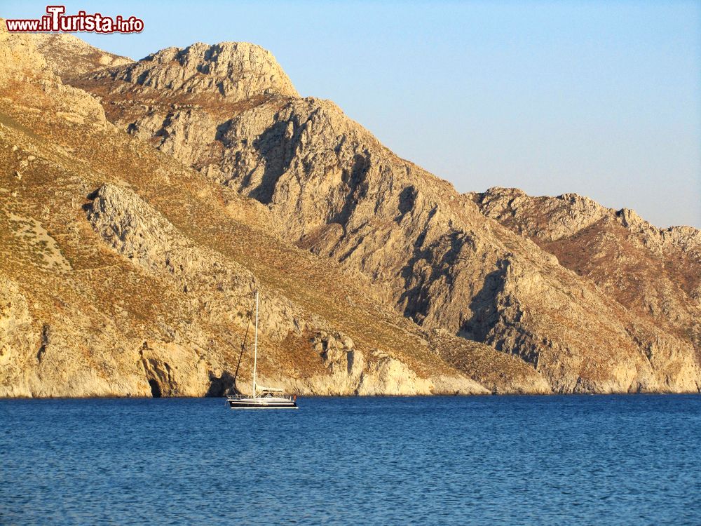 Immagine Un tratto della costa di Tilos lambita dalle acque blu del mare, Grecia. Selvaggio e roccioso, questo territorio greco ospita antiche vestigia. 