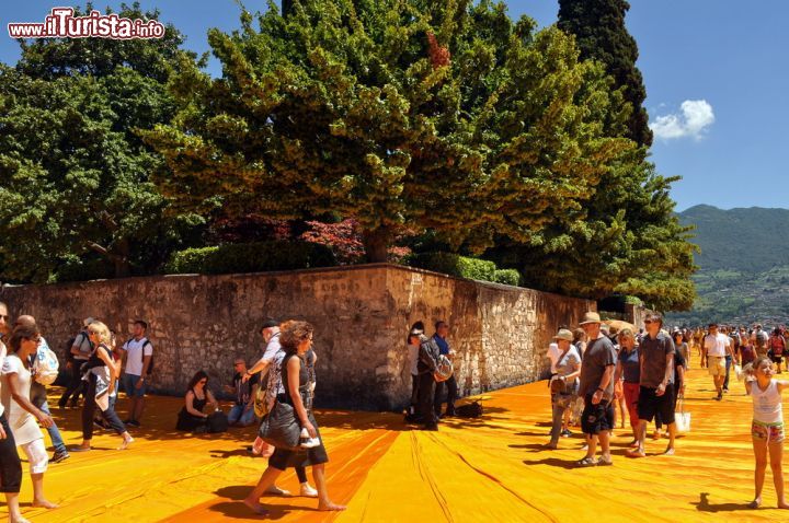 Immagine Turisti a Peschiera Maraglio fotografati mentre camminano sulle Floating Piers di Christo, nel tratto in cui costeggiano il Monte Isola sul Lago di Iseo - © s74 / Shutterstock.com