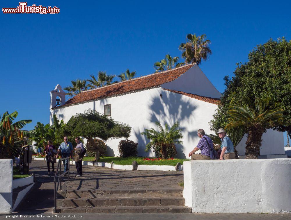 Immagine Turisti in visita a Puerto de la Cruz in una giornata di sole, Tenerife, Spagna. Sullo sfondo, una chiesetta intonacata di bianco - © Kristyna Henkeova / Shutterstock.com