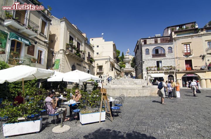 Immagine Turisti seduti nel dehors di un bar in Piazza del Duomo a Taormina, Sicilia. Raccolta e suggestiva, questa piazza di Taormina ospita al suo centro una fontana barocca in pietra dove si trova il simbolo cittadino, una figura mitologica per metà donna e metà toro. Qui, in uno dei tanti bar, ci si può fermare per assaporare qualche specialità tipica della Sicilia - © villorejo / Shutterstock.com