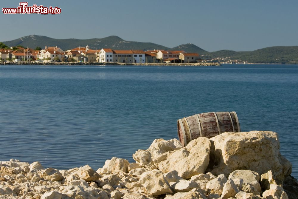 Immagine Un antico barile in legno fra le rocce del litorale nei pressi di Bibinje, Croazia. Sullo sfondo, il panorama della città.