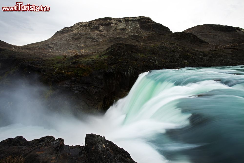 Immagine Un corso d'acqua con cascata a Puerto Natales, Cile. A fare da scenario, un paesaggio aspro e selvaggio.