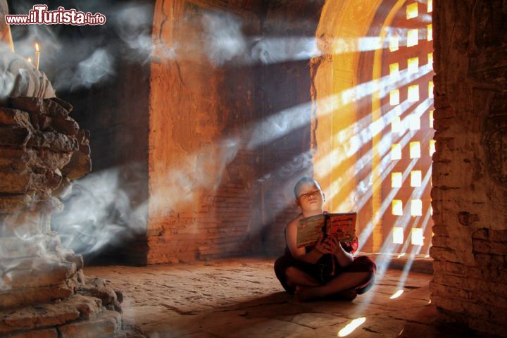 Immagine Un giovane monaco intento a leggere all'interno di una pagoda a Bagan, Myanmar. La luce soffusa che entra nella pagoda illumina le pagine del libro che questo giovane religioso buddista sta studiando - © pixy_nook / Shutterstock.com