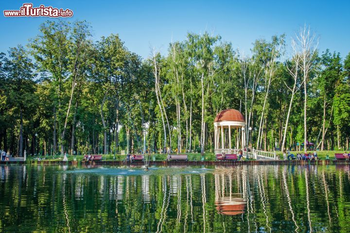 Immagine Un grazioso laghetto nel parco centrale di Kharkiv, Ucraina. Sulle calme acque del lago si riflettono gli alberi alti e slanciati che fanno da cornice alle panchine su cui riposarsi dopo una bella passeggiata