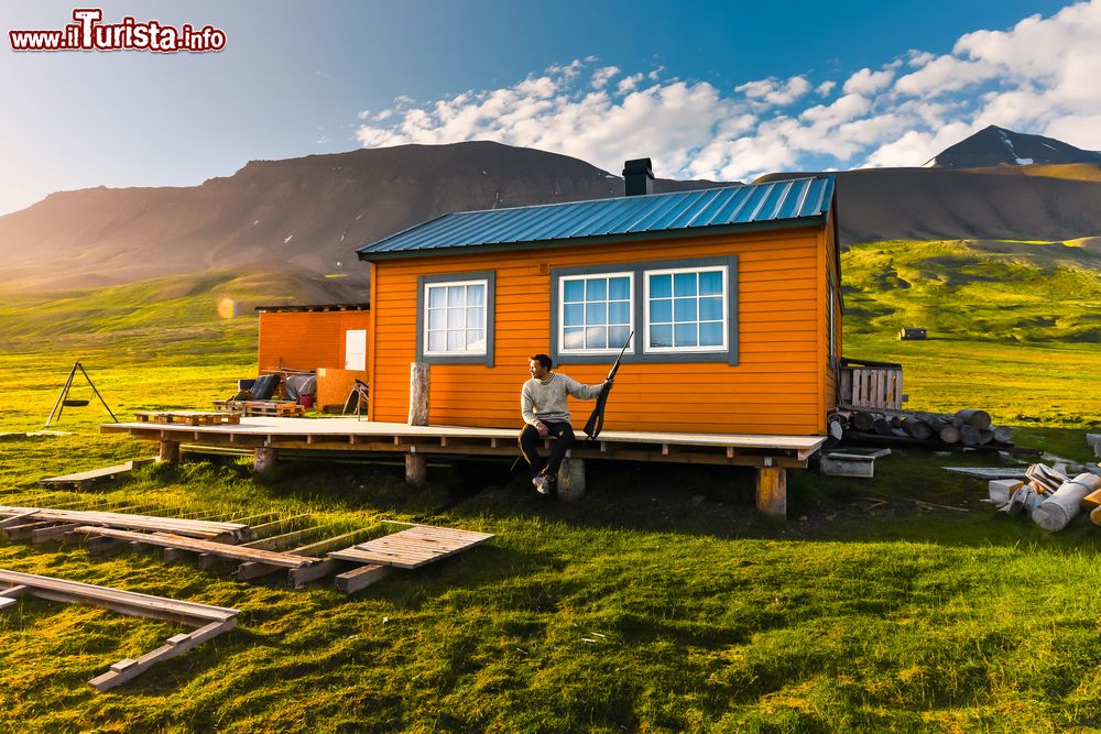 Immagine Un paesaggio naturale delle montagne di Spitsbergen a Longyearbyen, isole Svalbard, Norvegia. Un cacciatore, seduto davanti a una casetta in legno, osserva il tramonto dell'estate artica.