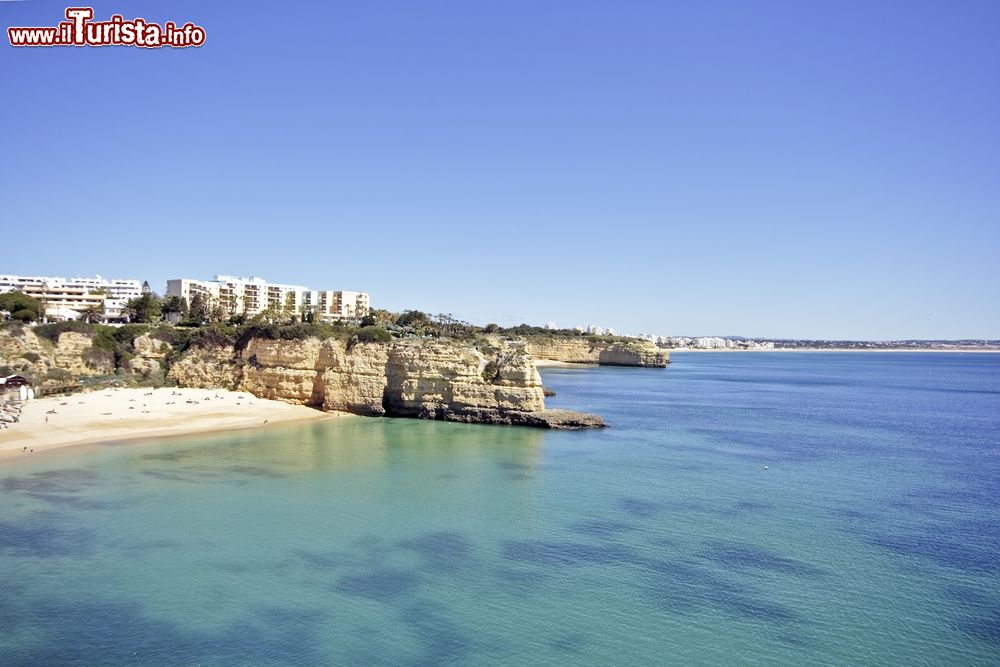 Immagine Un tratto di litorale a Armacao de Pera, Portogallo. Lasabbia dorata è lambita dall'acqua di un mare azzurro e sereno che si estende a perdita d'occhio.