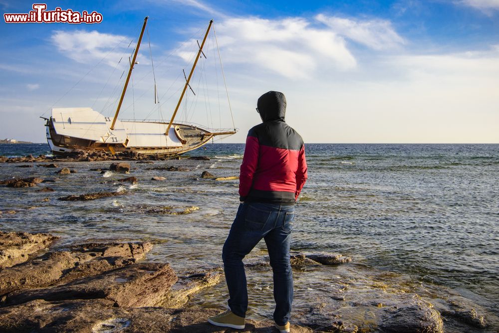 Immagine Un uomo osserva una barca naufragata dalla costa di Calasetta, Sardegna.