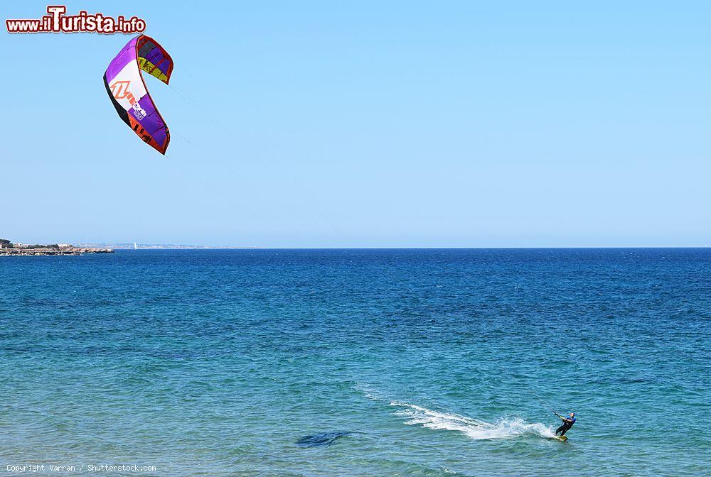 Immagine Un uomo pratica kitesurf nel tranquillo Mar Ionio a Avola, Sicilia. Questo sport acquatico nato nel 1999 consente di farsi trainare da un aquilone utilizzando il vento come propulsore - © Varran / Shutterstock.com