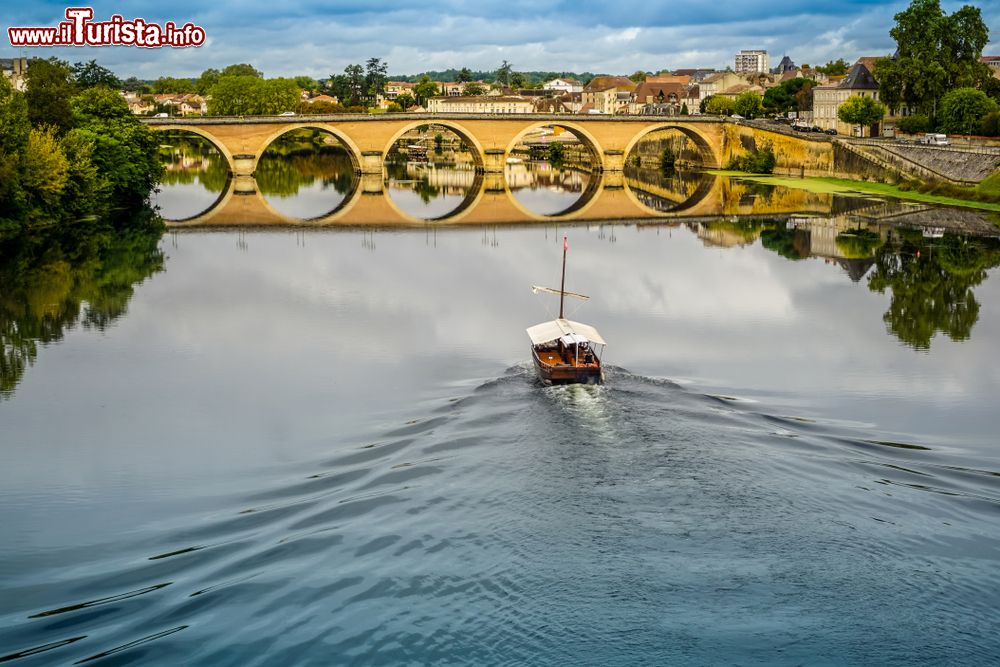 Immagine Una barca solca il fiume Dordogna a Bergerac, Francia. Sullo sfondo, il vecchio ponte che si riflette sull'acqua.