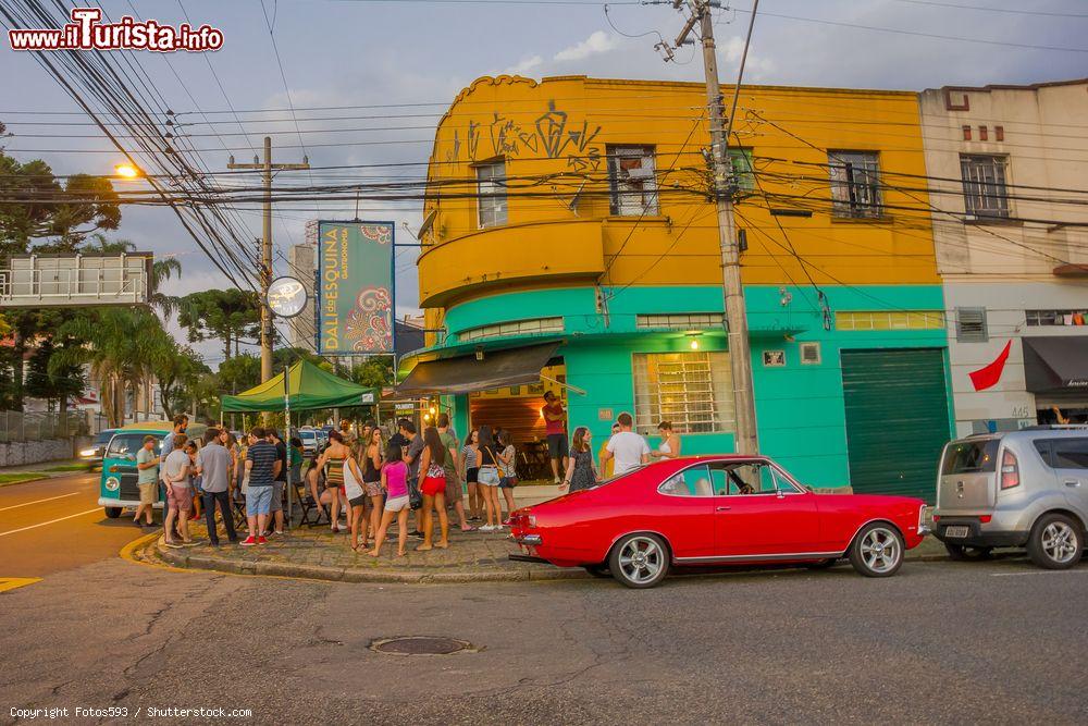 Immagine Una bella automobile rossa parcheggiata all'angolo di una strada a Curitiba, Brasile. Fuori da un ristorante la gente attende il proprio turno - © Fotos593 / Shutterstock.com