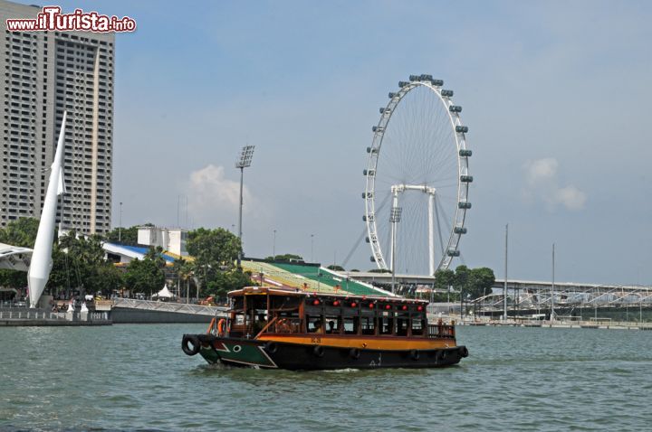 Immagine Una bumboat, tipica imbarcazione di legno a motore di Singapore, con la ruota panoramica sullo sfondo. Una volta arrivati a The Quays (i moli) ci si può imbarcare per una crociera di 40 minuti lungo il fiume Singapore da cui osservare il meraviglioso panorama della città passando per alcune delle sue principali zone turistiche - © Sonja Vietto Ramus