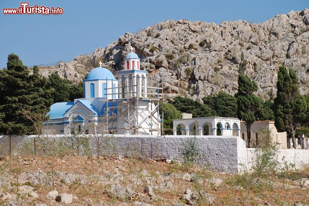 Immagine Una chiesetta con la cupola e il tetto azzurro al cimitero di Emborio, isola di Chalki (Grecia). Il campanile è sorretto da un'impalcatura per via di danni strutturali.