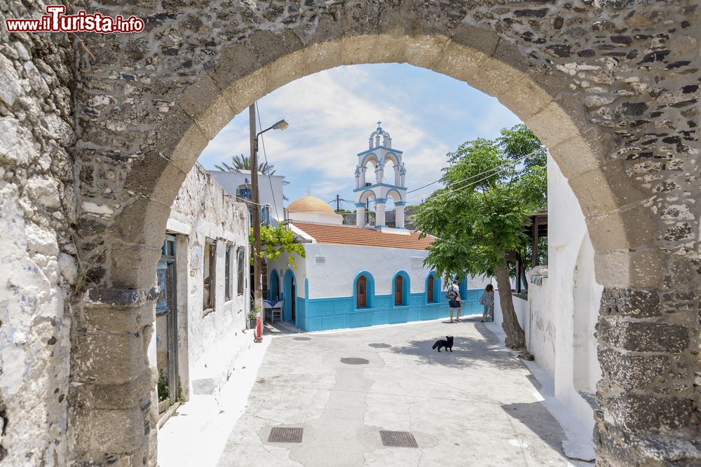 Immagine Una chiesetta del villaggio di Emporios, isola di Nisyros, vista da sotto un arco in pietra.