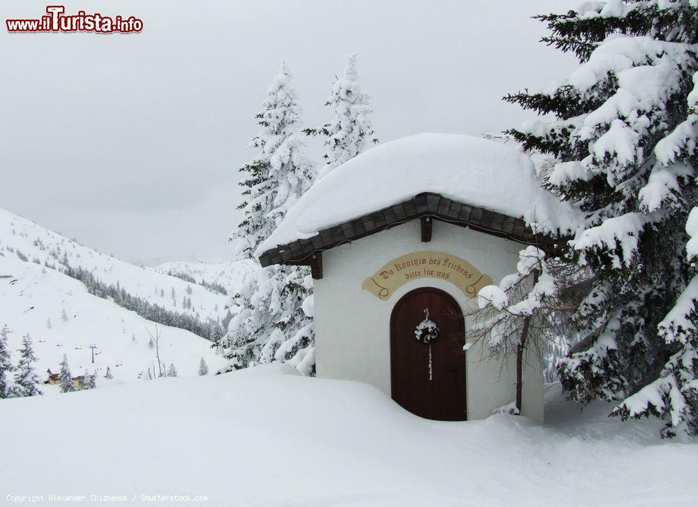 Immagine Una chiesetta innevata nello ski resort sulle Alpi austriache a Flachau. Sopra la porta si legge la scritta "Regina della Pace prega per noi" - © Alexander Chizhenok / Shutterstock.com