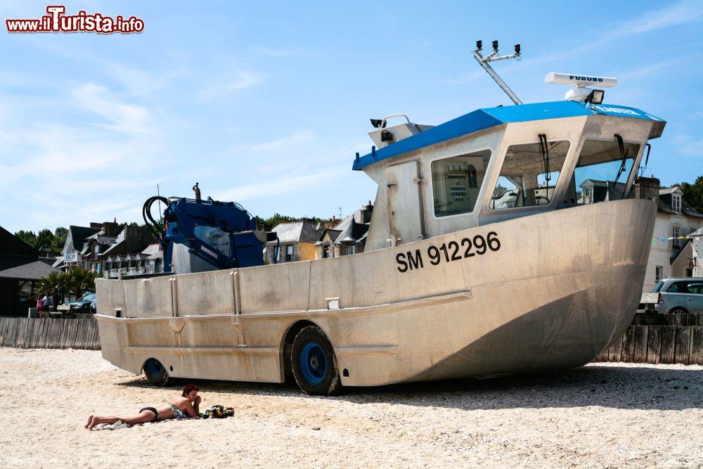 Immagine Una donna in relax  sulla spiaggia nei pressi del porto La Houle a Cancale, Francia.  Sullo sfondo, la nave anfibia della città - © vvoe / Shutterstock.com