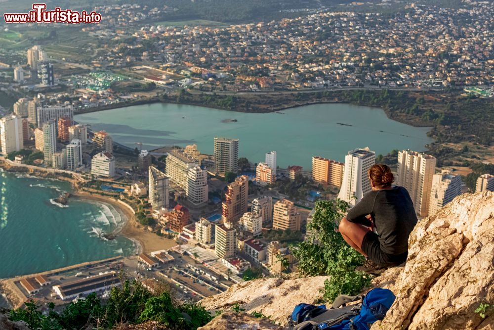 Immagine Una donna seduta su una collina del Penon de Ifach ammira la città di Calpe, Spagna.