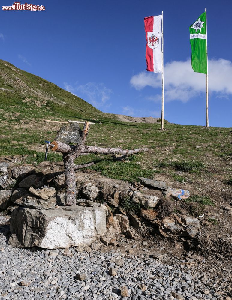 Immagine Una fontana di acqua potabile al rifugio Sillianer lungo il Carnic Peace Trail, Sillian (Austria). Sullo sfondo, la bandiera austriaca e quella del club alpino d'Austria.