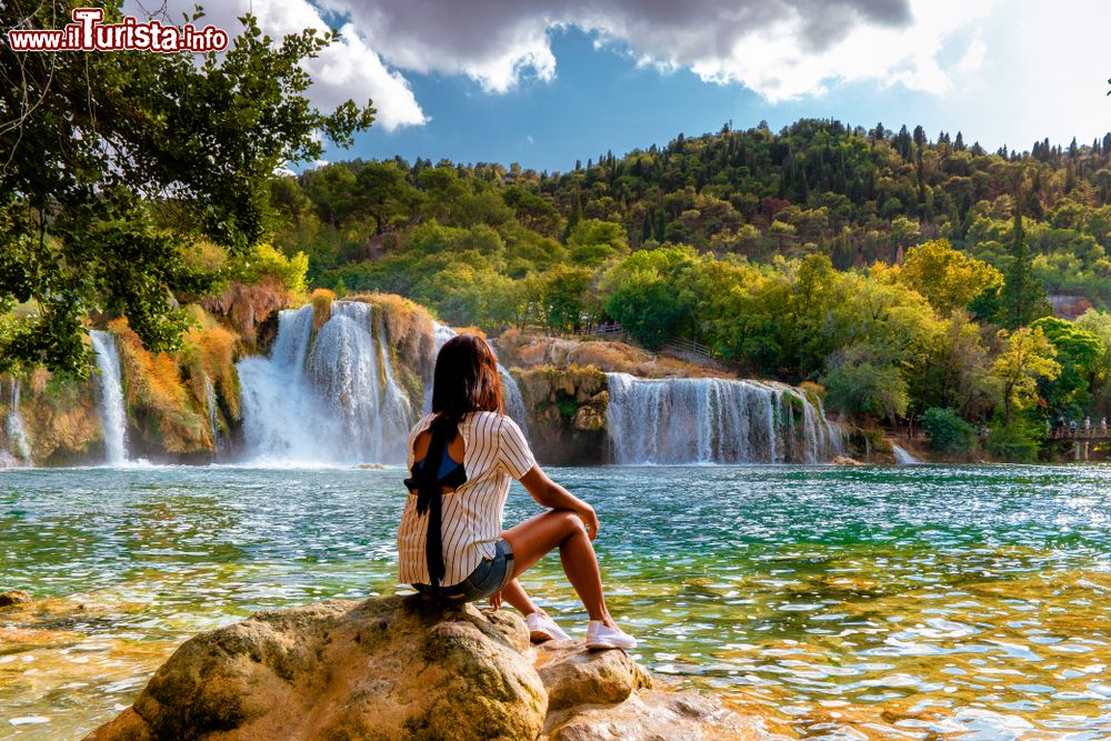 Immagine Una giovane donna ammira il paesaggio nel Krka National Park di Skradin, Croazia, in estate. Sullo sfondo, le cascate che rendono celebre questo luogo.