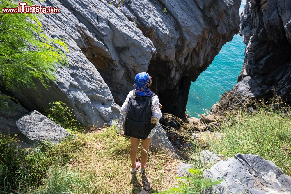 Immagine Una giovane donna fa trekking guardando il mare a Phra Nang, Thailandia. Le scogliere chiare si tuffano nel turchese chiaro delle acque cristalline.