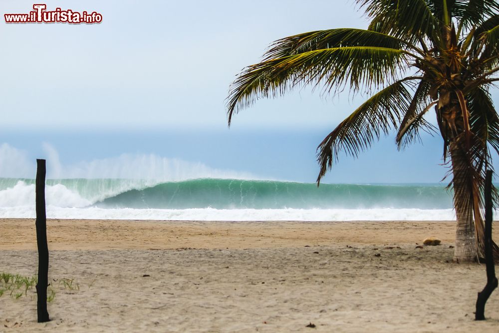 Immagine Una grande onda s'infrange sulla spiaggia di Puerto Escondido, Messico, in una giornata nuvolosa.